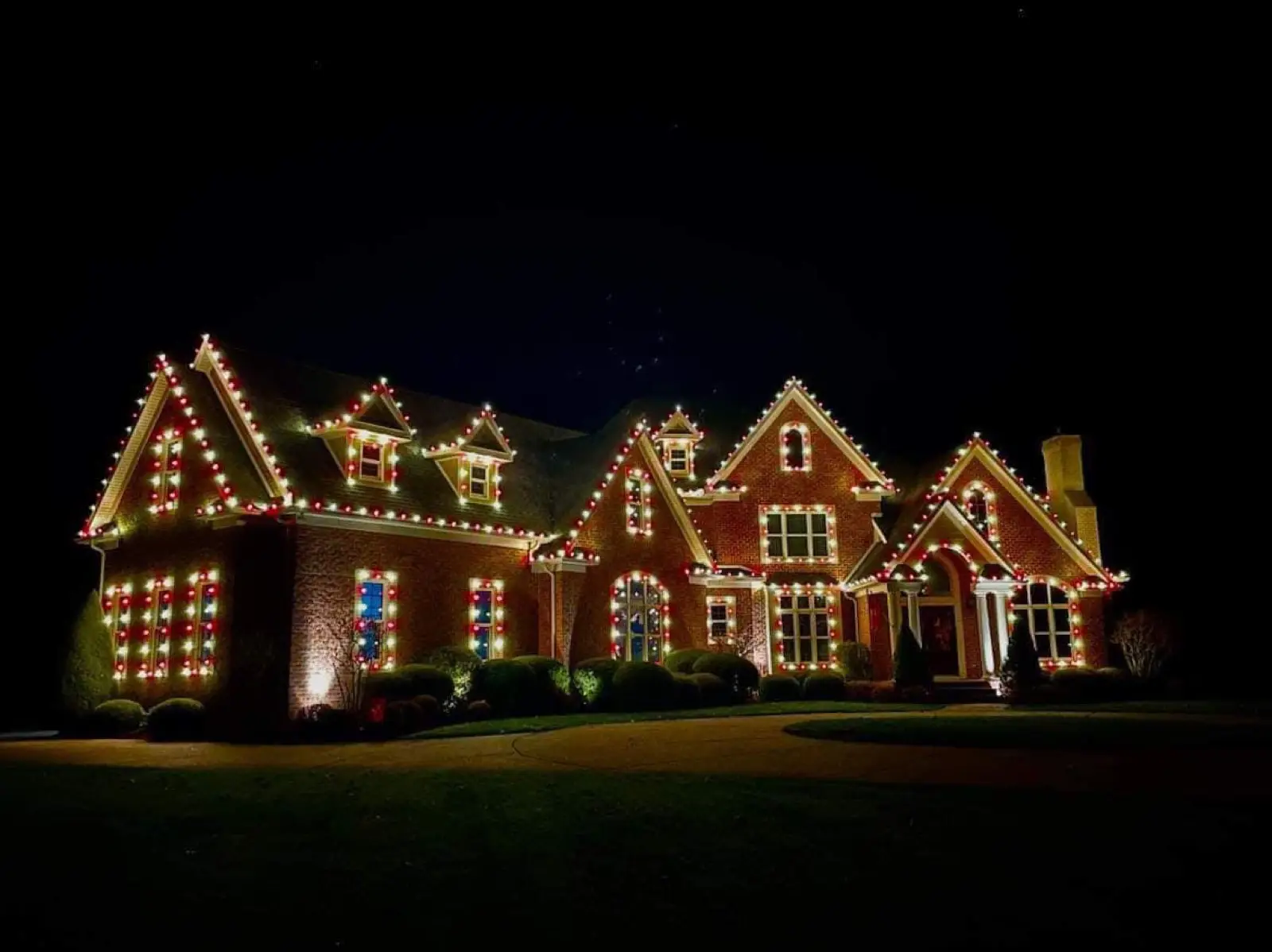 A brick estate outlined in alternating red and white bulbs with each window framed in lights