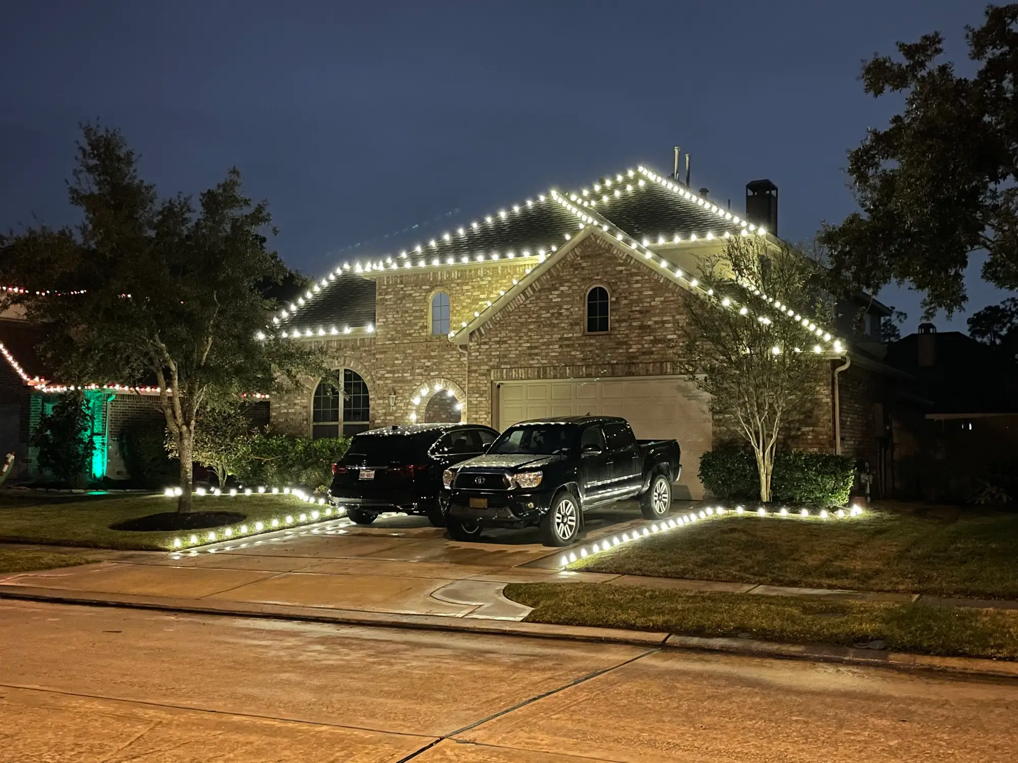 A two-story brick home with every roofline outlined in white C9 bulbs and the driveway and walkway lined with lights