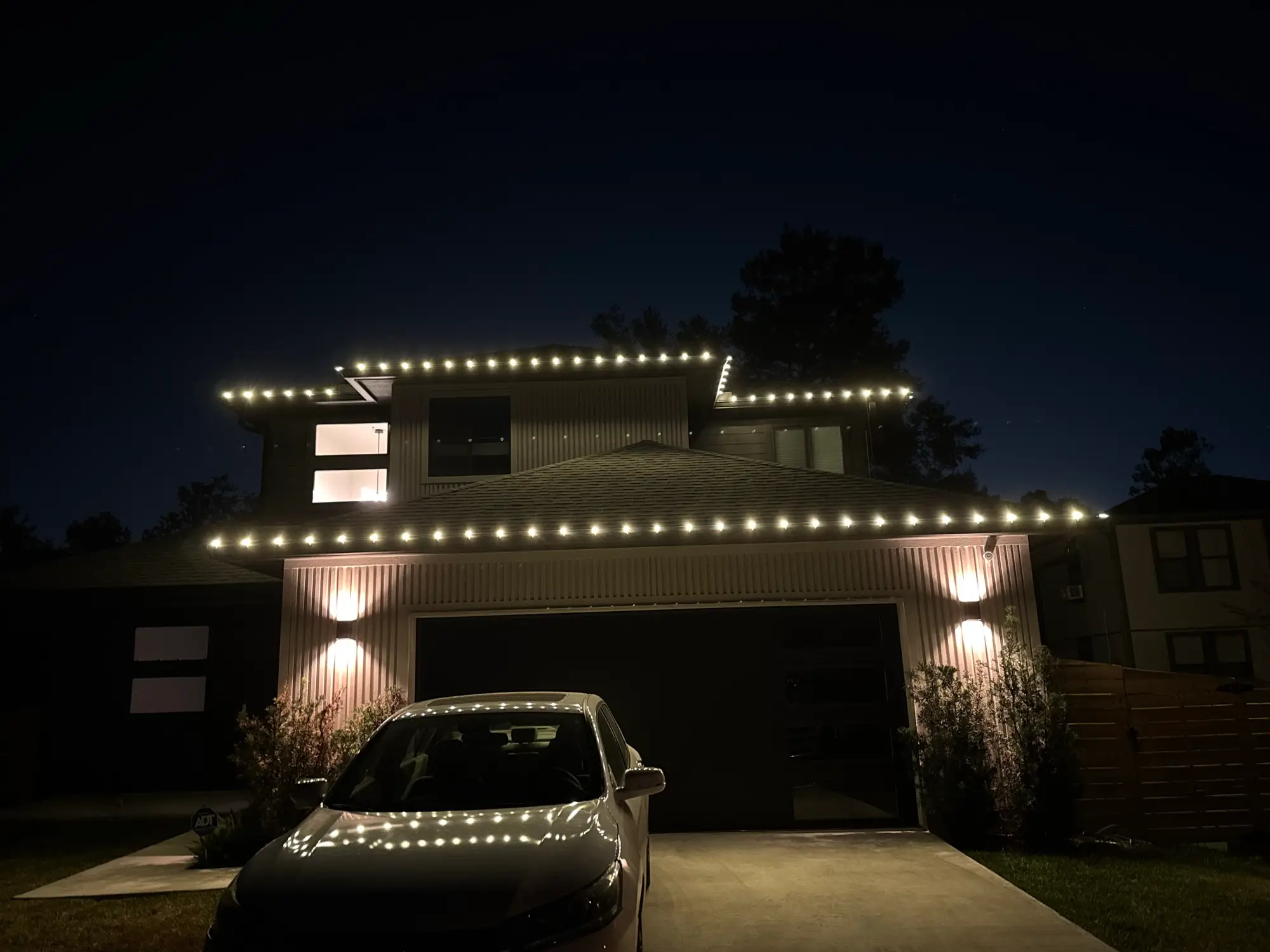 A modern two-story home with clean, evenly spaced warm white bulbs running the length of both rooflines