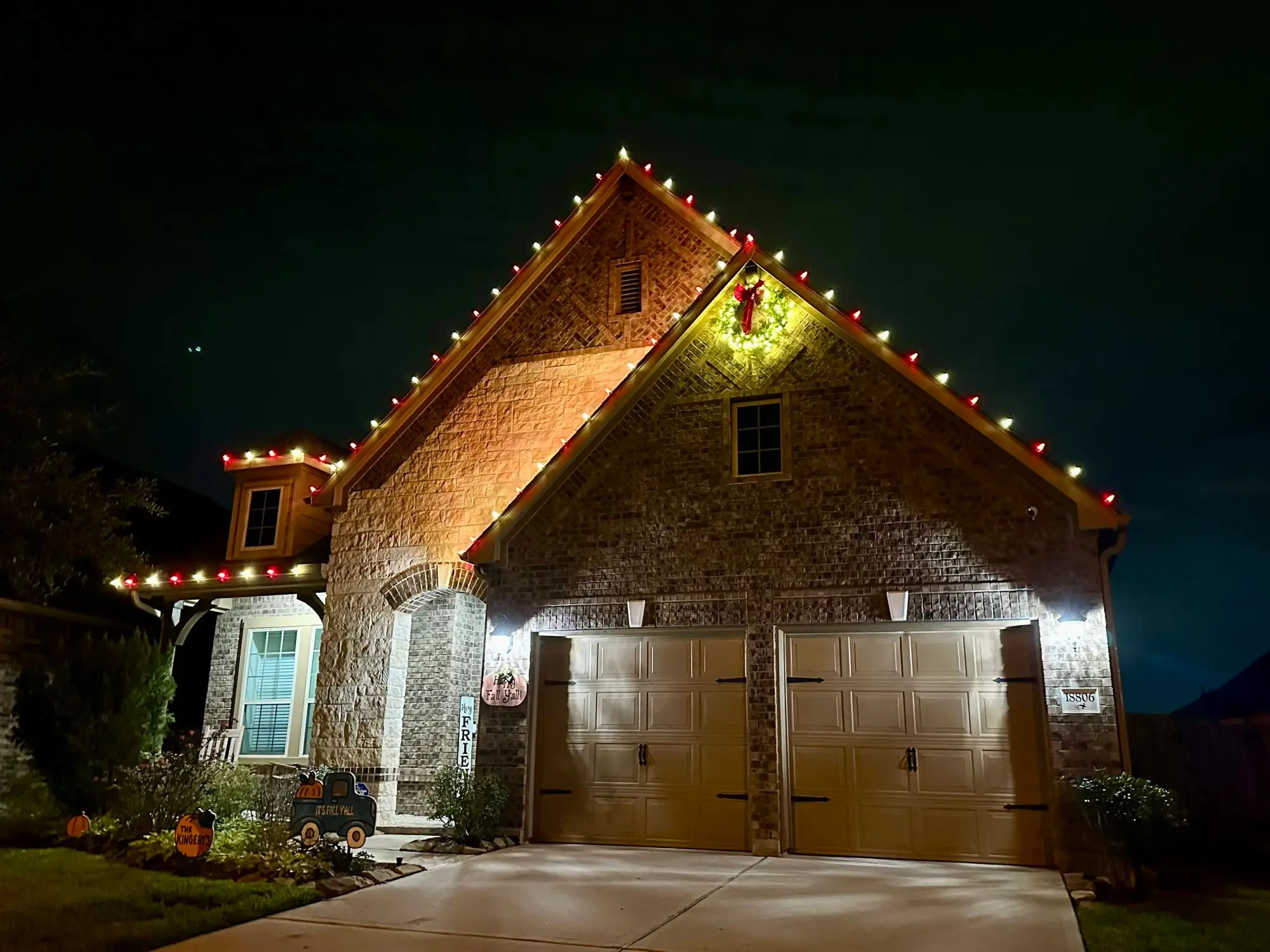 Alternating red and white C9 bulbs following the peaks of a brick home, with a lit wreath centred on the gable